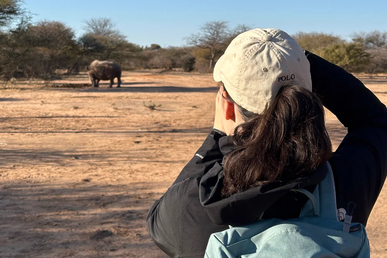 Guide and guest photographing rhino from a safari vehicle